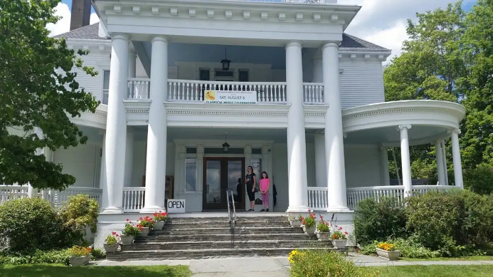 two women standing outside of a large white house